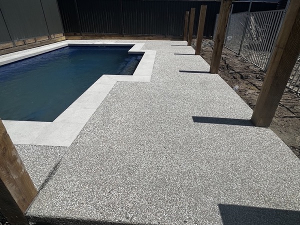 An exposed aggregate pool surround laid around a swimming pool with a timber-post fence line