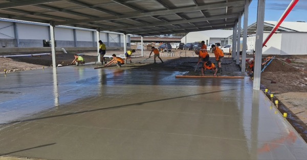 A crew in hi-vis working across a large commercial slab under a steel-framed roof