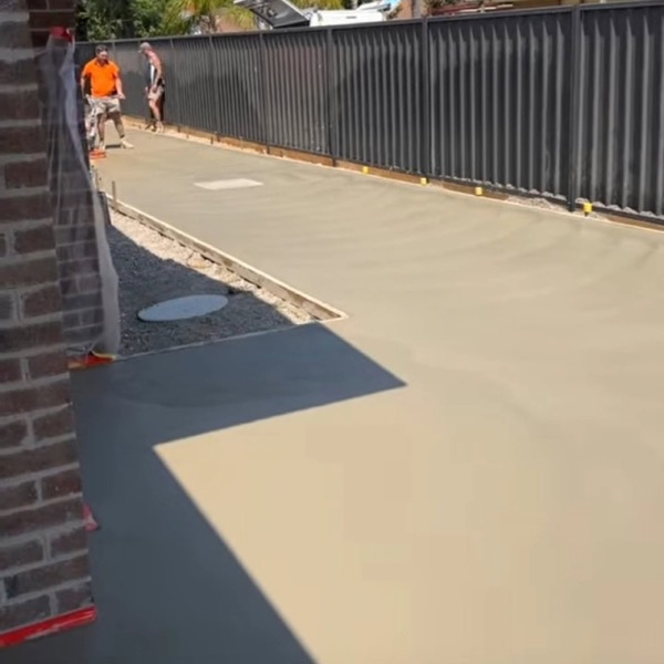 A freshly poured concrete path curving beside a brick wall