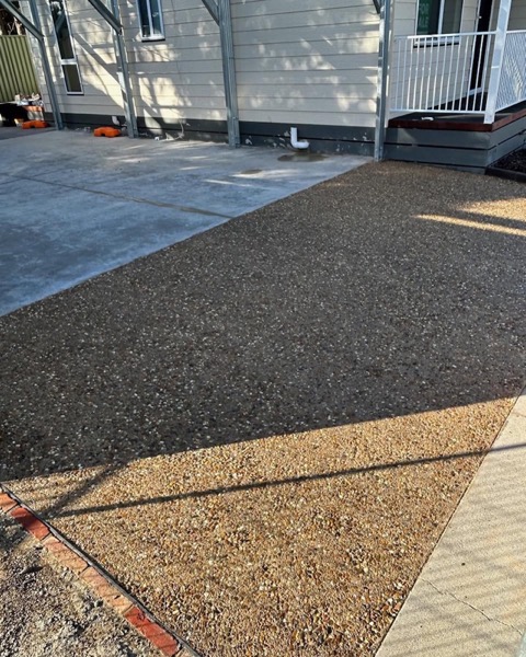 Exposed aggregate meeting a band of plain concrete beside a fence line
