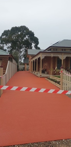 A terracotta coloured concrete driveway running past the verandah of a period brick home