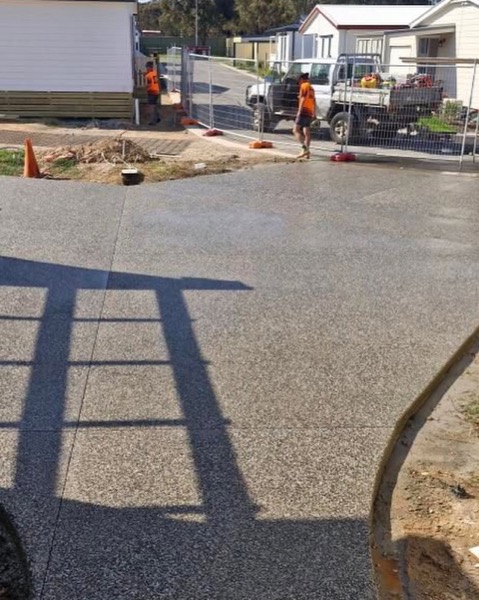 A finished concrete driveway with a work ute and crew at the far end