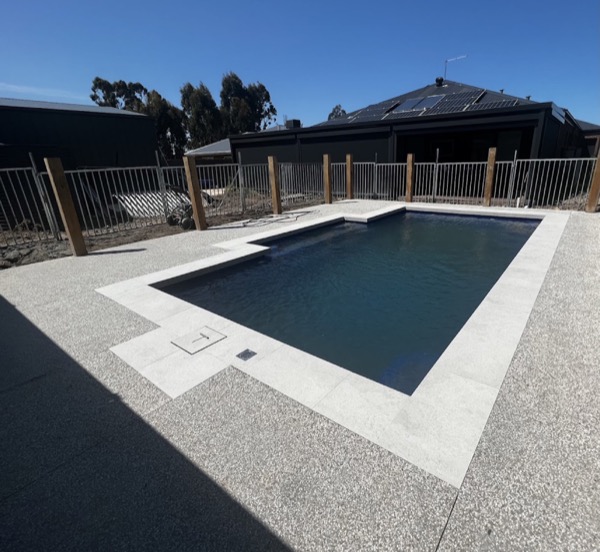 A pale exposed aggregate pool surround with paver coping at a new build