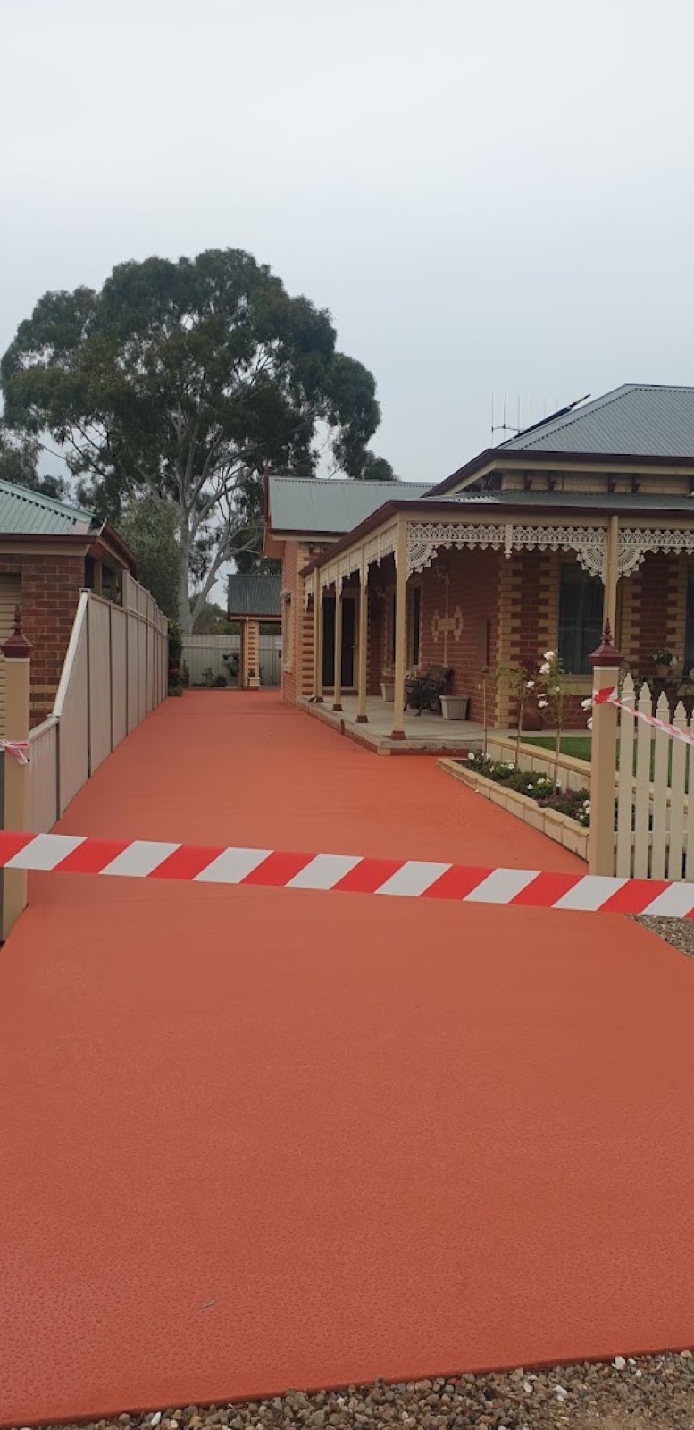 A terracotta coloured concrete driveway running past the verandah of a period brick home